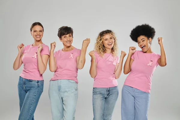 Обізнаність про рак молочної залози, схвильовані міжрасові жінки з рожевими стрічками на сірому, різноманітність, без раку — стокове фото