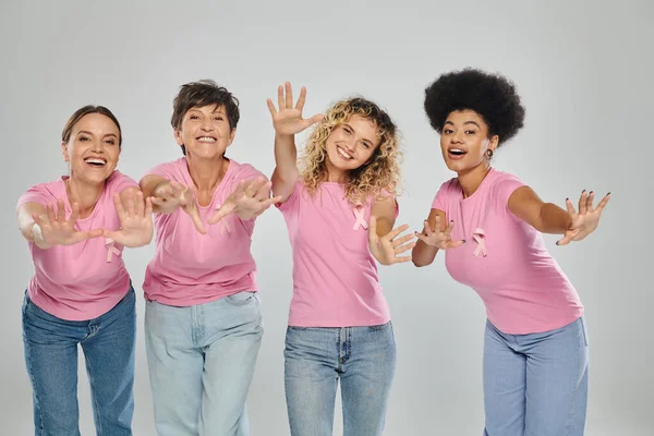 Breast cancer awareness, joyful interracial women with pink ribbons on grey, diversity, cancer free — Stock Photo