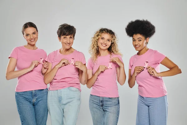 Concienciación sobre el cáncer de mama, alegres mujeres interracial tocando cintas rosas en gris, diversidad, concepto - foto de stock