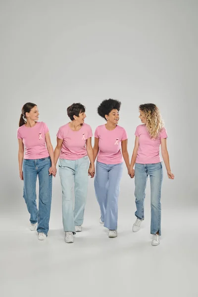 Brustkrebs-Bewusstsein, positive multikulturelle Frauen mit rosafarbenen Bändern, die gemeinsam auf grau laufen — Stockfoto