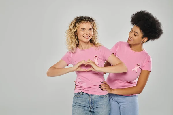 Concienciación sobre el cáncer de mama, alegres mujeres interracial con cintas rosas sobre fondo gris, diversidad - foto de stock