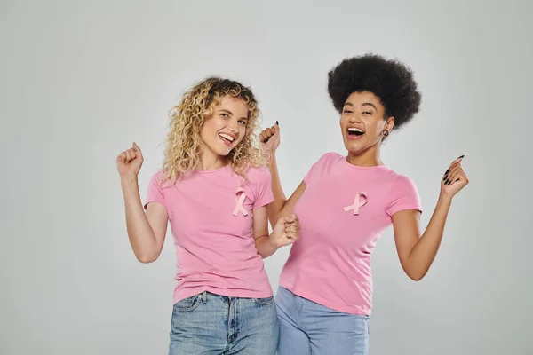 Concienciación sobre el cáncer de mama, mujeres multiculturales excitadas con cintas rosadas sobre fondo gris, sin cáncer - foto de stock