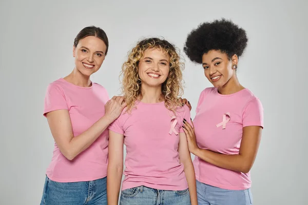 Осведомленность о раке молочной железы, счастливые четыре межрасовые женщины с розовыми лентами на сером фоне, разнообразные — стоковое фото