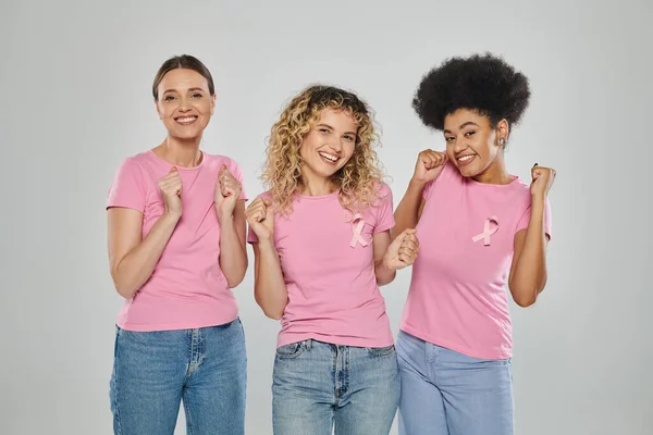 Осведомлённость о раке молочной железы, радостные межрасовые женщины с розовыми лентами на сером, разнообразие, отсутствие рака — стоковое фото