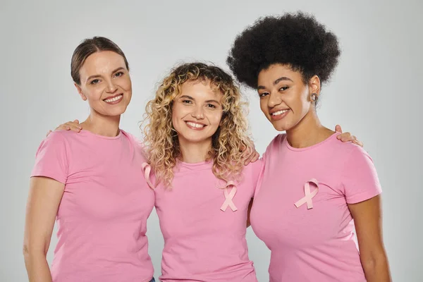 Breast cancer awareness, interracial women with pink ribbons on grey, diversity, smile, cancer free — Stock Photo