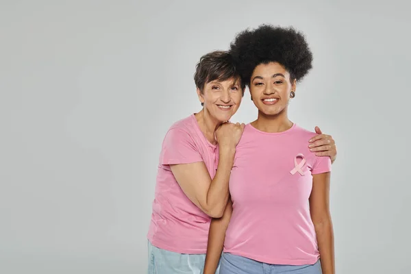 Concienciación sobre el cáncer de mama, mujeres multiculturales felices abrazándose en el telón de fondo gris, campaña de apoyo - foto de stock
