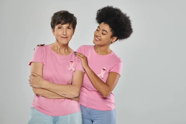 Concienciación sobre el cáncer de mama, alegres mujeres multiculturales sonriendo sobre fondo gris, apoyo, libre de cáncer - foto de stock