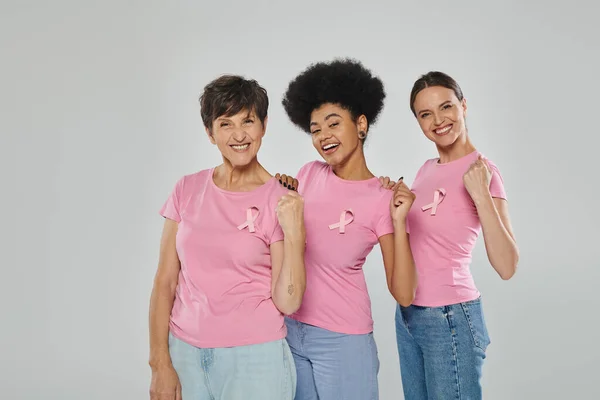 Sensibilisation au cancer du sein, joyeuses femmes multiculturelles souriant sur fond gris, différentes générations — Photo de stock