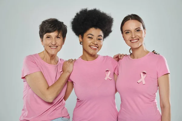 Concienciación sobre el cáncer de mama, mujeres interracial sonriendo sobre fondo gris, diferentes generaciones, retrato - foto de stock