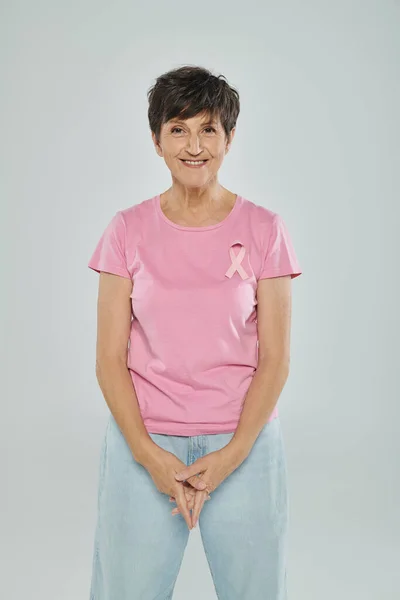 Brustkrebs-Bewusstsein, glückliche Frau mittleren Alters mit rosa Schleife, grauer Hintergrund, krebsfrei — Stockfoto
