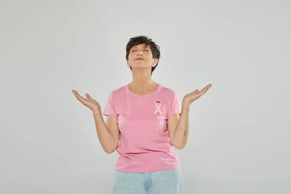 Осознание рака молочной железы, счастливая зрелая женщина с розовой лентой, серый фон, радость, медитация — стоковое фото