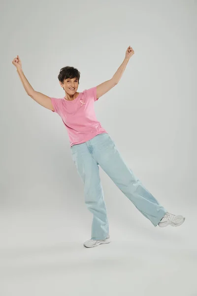 Breast cancer awareness, happy mature woman with pink ribbon, grey backdrop, emotional gesturing — Stock Photo