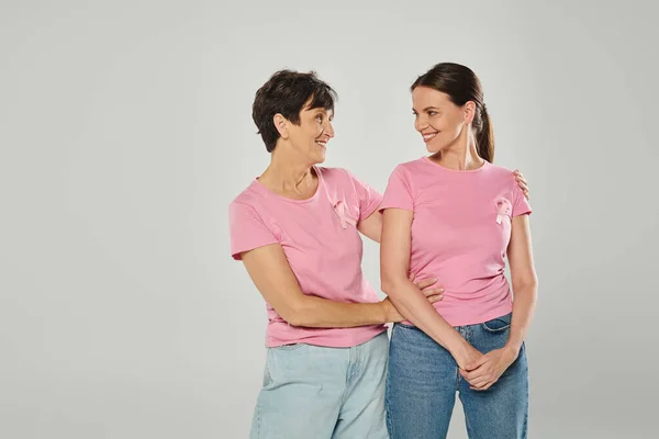 Donne con nastri rosa sorridenti, sfondo grigio, abbraccio, generazioni diverse, consapevolezza del cancro al seno — Foto stock