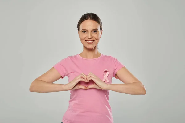 Donna felice con nastro rosa, sfondo grigio, consapevolezza del cancro al seno, cancro libero, segno del cuore — Foto stock