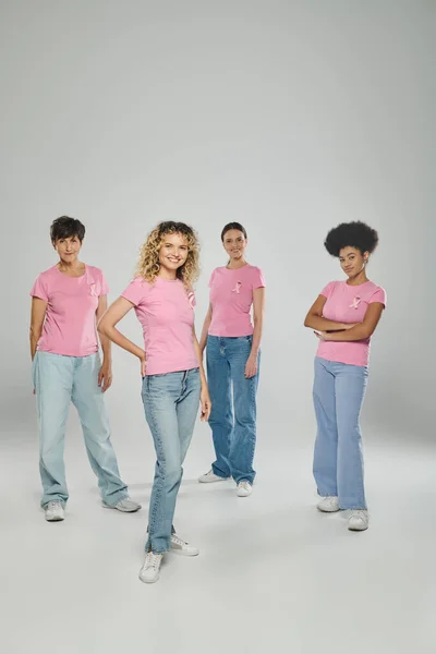 Cheerful interracial women different age standing on grey backdrop, breast cancer awareness, unity — Stock Photo