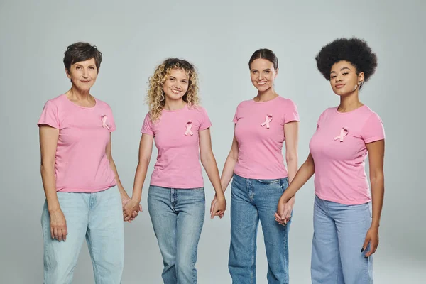 Donne interrazziali di età diversa che si tengono per mano su sfondo grigio, supporto, consapevolezza del cancro al seno — Foto stock
