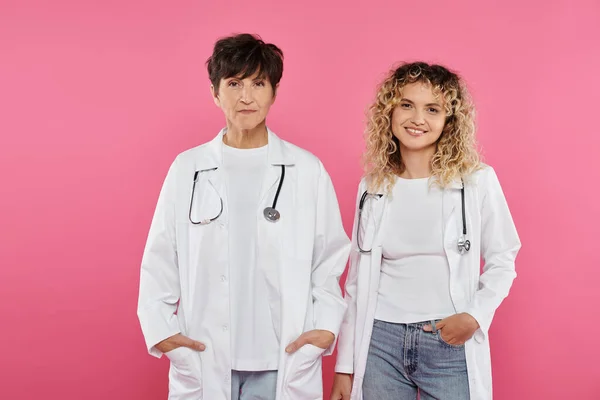 Médicos felizes do sexo feminino em casacos brancos em pé no fundo rosa, sorriso, consciência do câncer de mama, mulheres — Fotografia de Stock