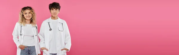Happy doctors in white coats standing on pink backdrop, women, joy, breast cancer awareness, banner — Stock Photo