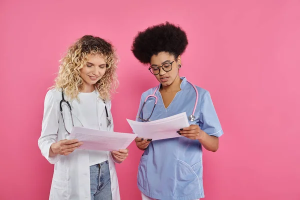 Happy female oncologists, interracial doctors on pink backdrop, breast cancer awareness, diagnosis — Stock Photo