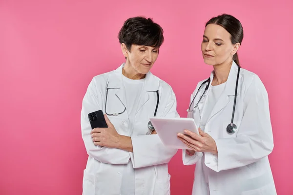 Oncólogos femeninos, médicos que usan aparatos, teléfonos inteligentes y tabletas, concepto de conciencia sobre el cáncer de mama - foto de stock