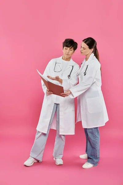 Онкологи, жінки-лікарі, які дивляться на папку, медичні записи, обізнаність про рак молочної залози, кампанія — стокове фото