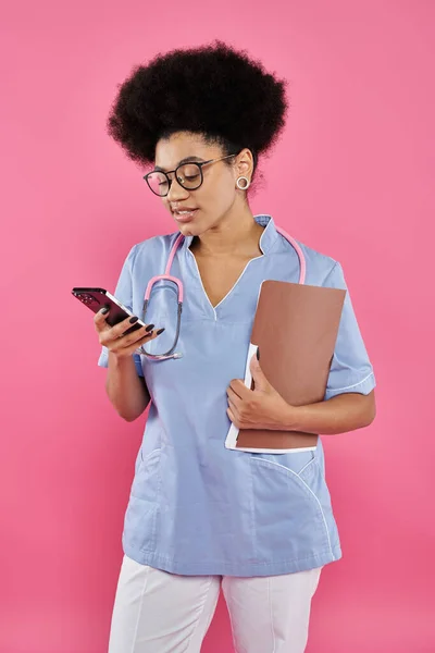 Consapevolezza del cancro al seno, medico afroamericano, felice oncologo con cartella utilizzando smartphone — Foto stock