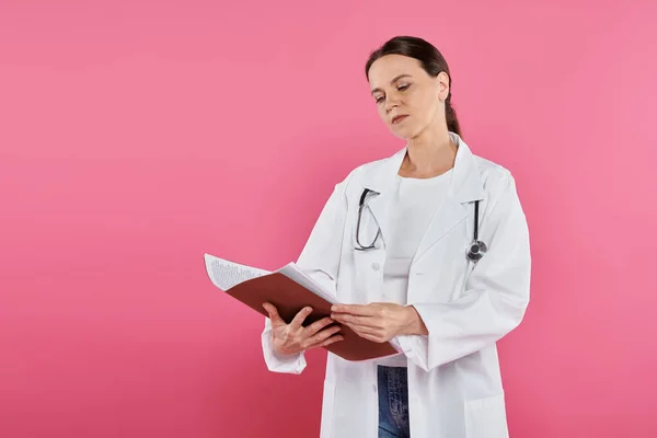 Breast cancer awareness, female doctor, oncologist reading medical record, folder, pink backdrop — Stock Photo