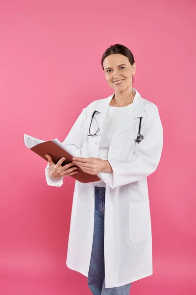 Осведомлённость о раке молочной железы, женщина-врач, счастливый онколог, читающий медицинскую карту, папку, розовый — стоковое фото
