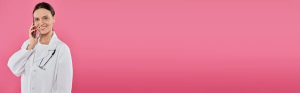 Medico sorridente parlando su smartphone mentre in piedi isolato su rosa, banner, concetto di cancro al seno — Foto stock