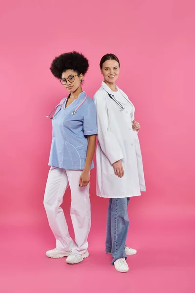 Médecins interracial joyeux regardant la caméra sur rose, concept de sensibilisation au cancer du sein — Photo de stock