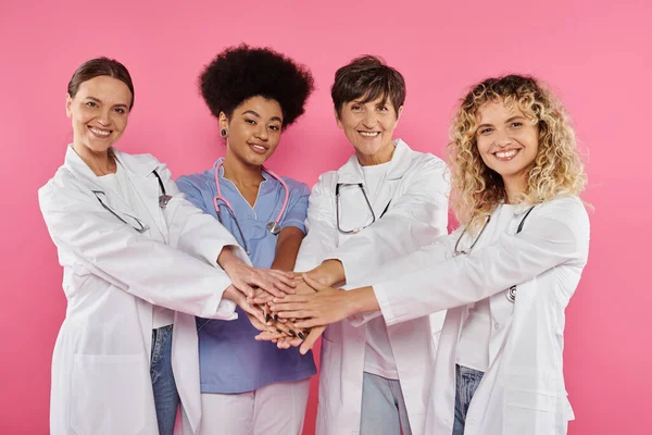 Groupe d'oncologues multiethniques joyeux tenant la main isolé sur rose, concept de cancer du sein — Photo de stock