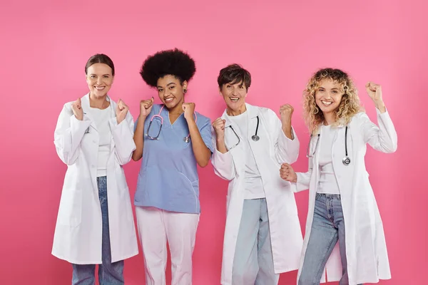 Група збуджених багатоетнічних онкологів, що показують так жест ізольовано на рожевому, місячному раку молочної залози — стокове фото