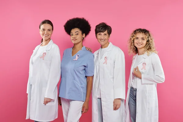 Sourire interracial médecins avec des rubans regardant caméra isolée sur rose, concept de cancer du sein — Photo de stock