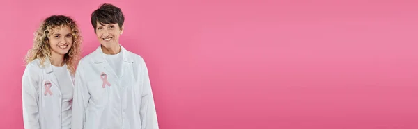 Улыбающиеся врачи с лентами на белых халатах, изолированных на розовый, баннер, рак груди концепции — стоковое фото