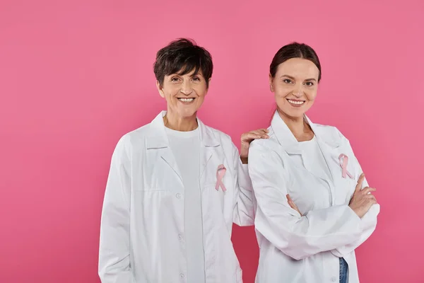 Médecins positifs avec des rubans posant et debout isolés sur rose, concept de cancer du sein — Photo de stock