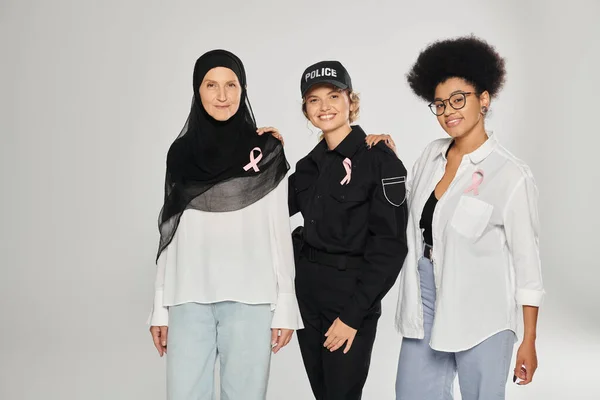 Mujeres interraciales positivas y diferentes con cintas rosadas de cáncer de mama aisladas en gris - foto de stock