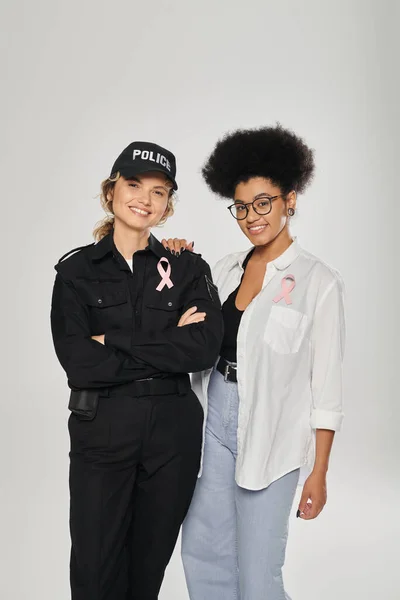 Mujeres interracial positivas con cintas de conciencia sobre el cáncer de mama aisladas en gris - foto de stock