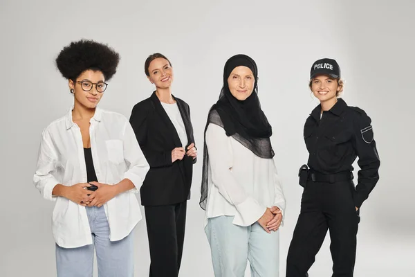 Grupo de mulheres multiétnicas olhando para a câmera e sorrindo enquanto posando isolado no cinza — Fotografia de Stock