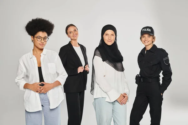 Group of multiethnic women looking at camera and smiling while posing isolated on grey — Stock Photo