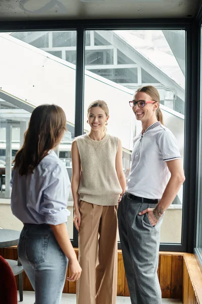 Tres colegas sonrientes discutiendo algo y riendo con el telón de fondo de la ventana, concepto de coworking - foto de stock