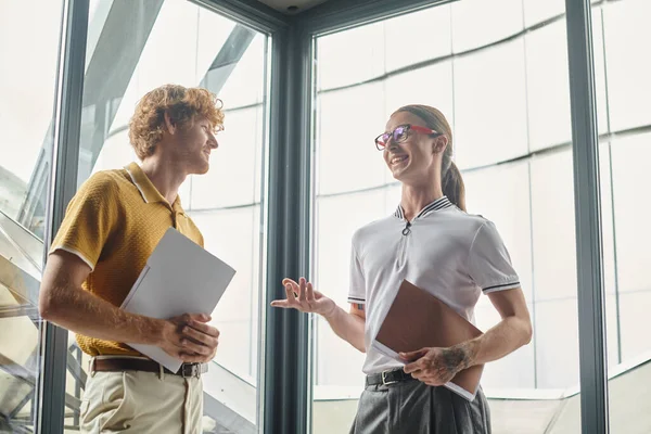 Two young coworkers with documents discussing work and looking at each other, coworking concept — Stock Photo
