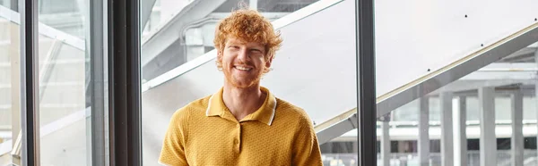 Cheerful ginger man smiling sincerely looking at camera with window on background, coworking, banner — Stock Photo