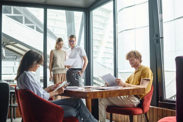 Four colleagues in business casual outfits working with papers in coworking, collaboration — Stock Photo