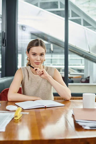 Young attractive woman with ponytail working on her papers and looking at camera, coworking concept — Stock Photo