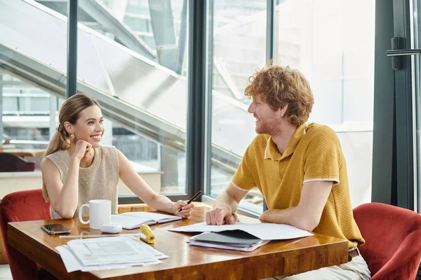 Two cheerful coworkers at table working on their paperwork and looking at each other, coworking — Stock Photo
