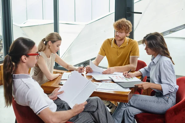 Four young coworkers in smart outfits highly focused on their working papers, coworking concept — Stock Photo