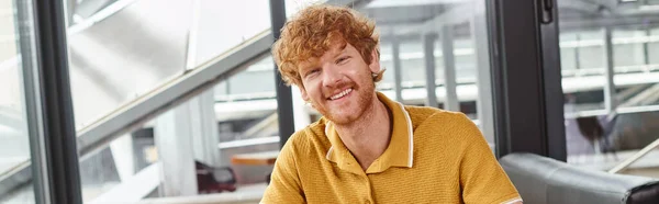 Счастливый рыжий волосатый мужчина улыбается и смотрит на камеру с задним стеклом, концепция коворкинга, баннер — стоковое фото