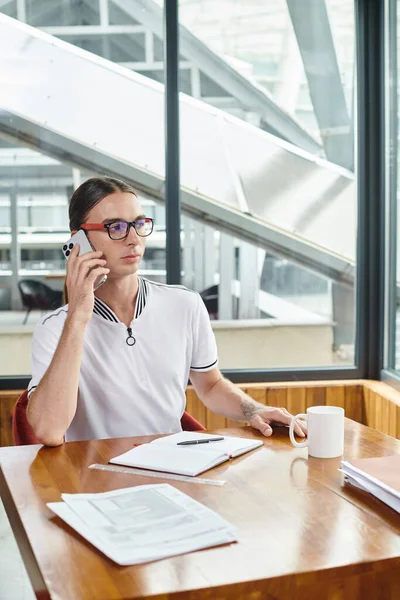 Ernsthafter, konzentrierter Mitarbeiter, der mit seinen Papieren arbeitet und am Tisch telefoniert, Coworking — Stockfoto