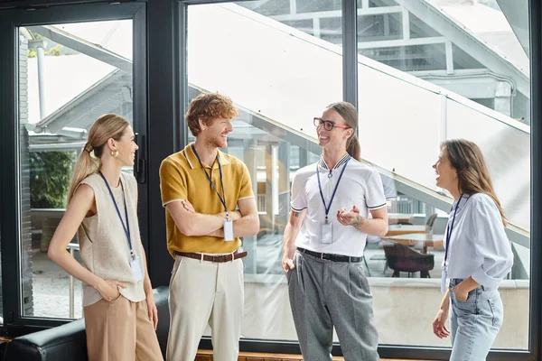 Cuatro jóvenes empleados en trajes informales inteligentes sonriendo sinceramente discutiendo el trabajo, el concepto de coworking - foto de stock