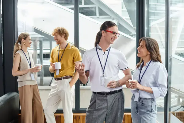 Cuatro compañeros de trabajo alegres en ropa inteligente sonriendo entre sí en la pausa del café, concepto de coworking - foto de stock
